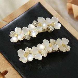 Detail view of two floral hair clips with white resin petals and golden metal base