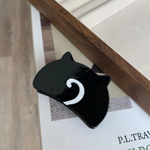 Detail view of a black cat-shaped acetate hair claw clip on a stylish wooden tray