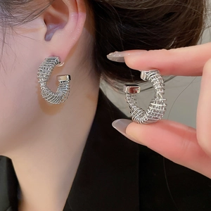 Close-up of silver-plated twisted C-shape earrings featuring a polished spiral texture