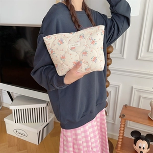 Quilted floral makeup bag with small orange flowers and a zip closure held by a model