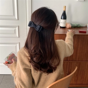Elegant black fabric bow hair clip worn on long wavy hair in a cozy interior setting