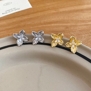 Detail shot of gold and silver four-petal flower earrings with inlaid cubic zirconia studs