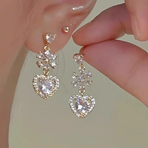 Close-up of golden heart and snowflake earrings with sparkling zircon gemstones