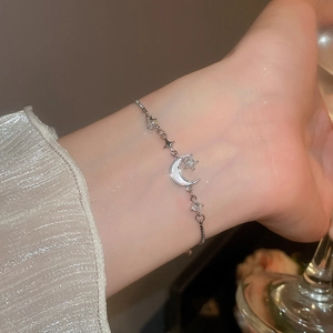 Nahaufnahme von Armband mit Mond und Stern Anhänger und Perlmutt am Handgelenk einer Frau
