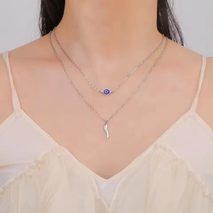 Close-up of double-layer silver necklace with blue evil eye bead and horn charm