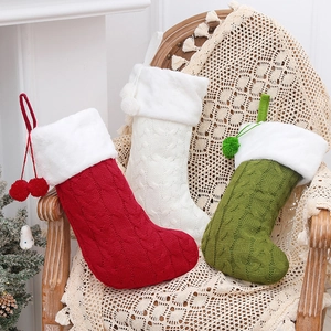 Three cable-knit Christmas stockings in red white and green with plush cuffs on a chair