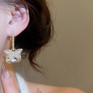 Close-up of golden butterfly earrings with rectangular zircon stone worn by a model