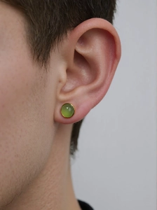 Close-up of elegant gold stud earring with green round gemstone worn by a model