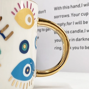 Detail of ceramic coffee cup with golden handle and blue evil eye patterns