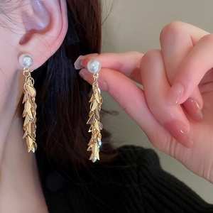 Detailed view of long gold leaf tassel earrings with white round imitation pearls