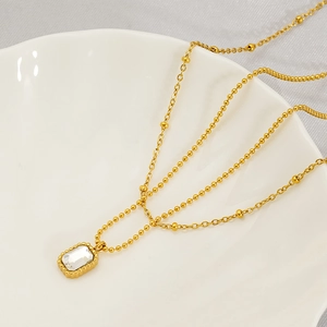 Mehrlagige goldene Perlenkette mit rechteckigem Zirkon-Anhänger auf Keramikschale