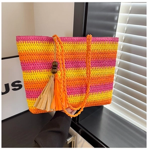 Detail view of woven straw tote featuring colorful stripes and bohemian tassel ornament