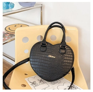 Détail d'un sac à main noir en forme de cœur avec motif crocodile sur chaise jaune