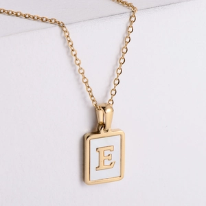 Detailed close-up of 18k gold plated square pendant with white shell inlay and letter E