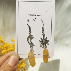 Close-up of handmade asymmetrical sun and moon earrings with wire-wrapped yellow stones