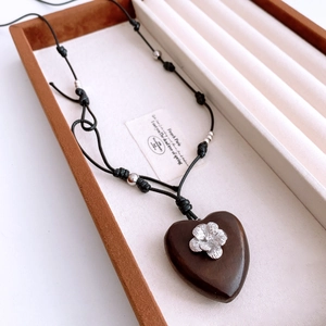 Detail of wooden heart pendant with silver flower on adjustable black woven cord necklace