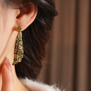 Détail de boucles d'oreilles vintage à pompons dorés et strass colorés sur un modèle