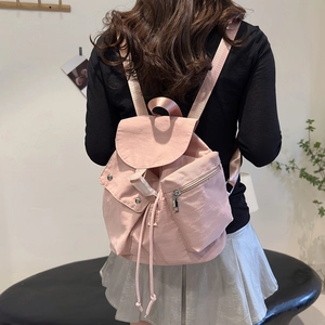 Detail of pink nylon backpack featuring drawstring closure, flap cover and side zipper pockets