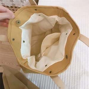 Close-up of mustard canvas tote interior featuring a metal magnetic buckle and inner pocket