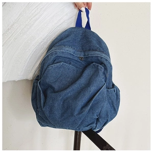 Close-up of blue denim backpack showing front zipper pocket and sturdy top handle