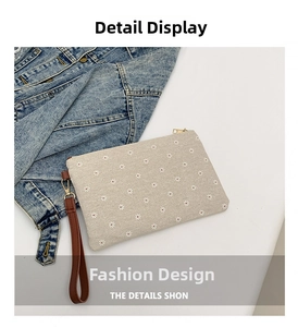 Detail of beige straw clutch with white daisy prints and a brown leather wristlet strap