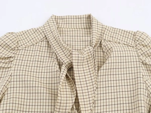 Detail of a beige and brown plaid women shirt featuring a tie-knot bow neckline design