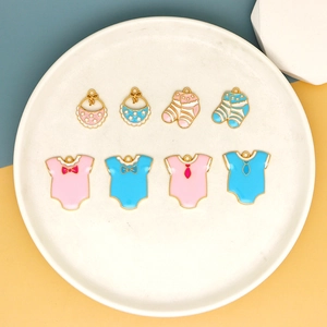 Detail of pink and blue enamel baby charms including bibs, socks, and rompers on a white plate