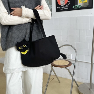 Close-up of black cat canvas tote bag showing yellow embroidered eyes and cat ear shape
