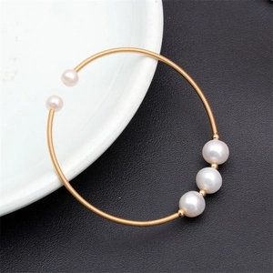 Detail of gold spiral cuff bracelet with five natural freshwater pearls on ceramic plate