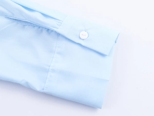 Macro shot of light blue cotton shirt cuff featuring a single white button and fine texture