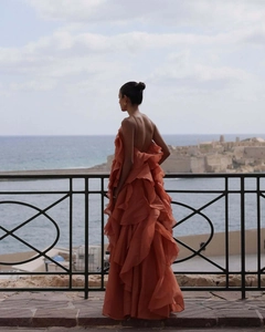 Back view of backless orange chiffon maxi dress with layered ruffles on seaside background