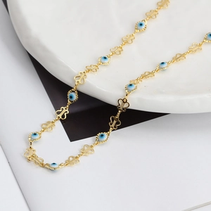 Detail of gold butterfly link chain with blue evil eye enamel beads on white tray