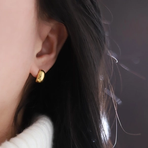 Modern gold bean-shaped oval earrings in polished titanium steel worn by a model