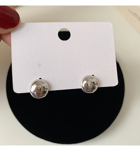 Macro detail of high-polish silver ball stud earrings on a white display card