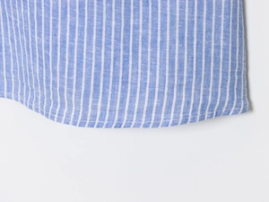 Détail macro de l'ourlet arrondi et des surpiqûres précises sur la chemise en coton à rayures