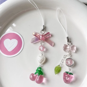 Detail view of pink translucent cherry and strawberry phone charms in a white ceramic dish