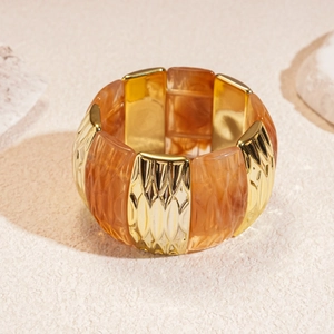 Close-up of a wide elastic bracelet featuring gold metal and amber resin square blocks