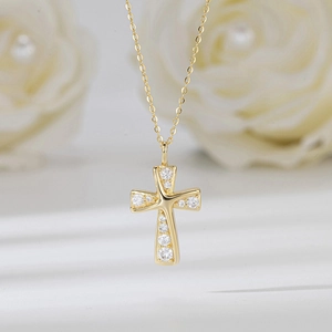 Gros plan du collier croix dorée avec pierres précieuses sur fond de roses blanches