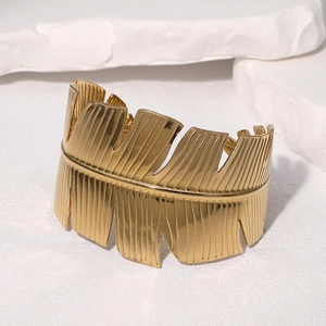 Polished 18k gold plated stainless steel wide leaf cuff bracelet on a white stone base