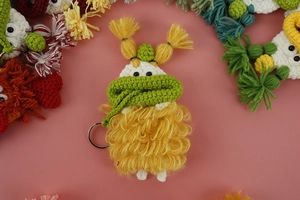 Macro shot of hand-knitted yellow monster keychain with green scarf and silver ring