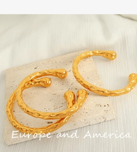 Detail showing two gold hammered open bangles with lava texture on stone tray