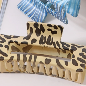 Close-up of a large leopard print hair claw clip with a blue striped hair accessory detail