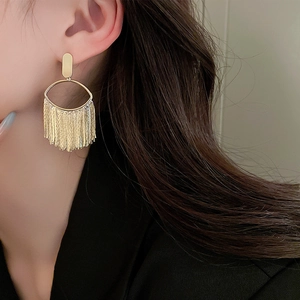 Close-up of gold-plated oval earrings with long metal tassels on model's ear