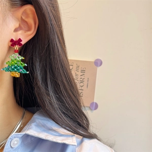 Detail of a handmade beaded Christmas tree earring with a red velvet bow on a model