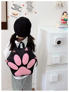 Detail shot of a black and pink cat paw backpack worn by a child in an indoor setting