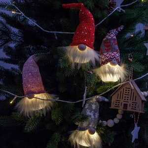 Hanging glowing Christmas gnomes ornaments with LED lights on a festive holiday tree