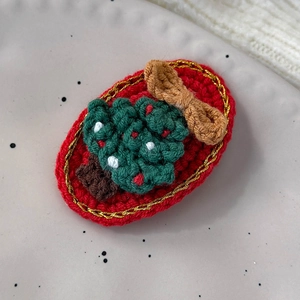 Close-up of a handmade crochet Christmas tree hair clip on a decorative plate