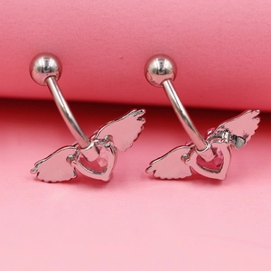 Détail de piercings de nombril en argent avec ailes de cœur rose sur fond rose vif