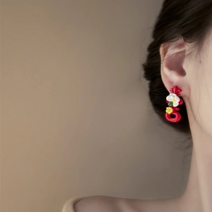 Macro view of red floral stud earrings with small white flowers and gold center detail