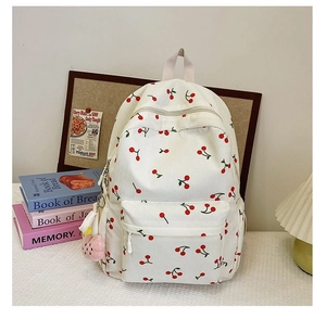 Close-up of cream corduroy backpack with cherry pattern and pink plush charm accessory